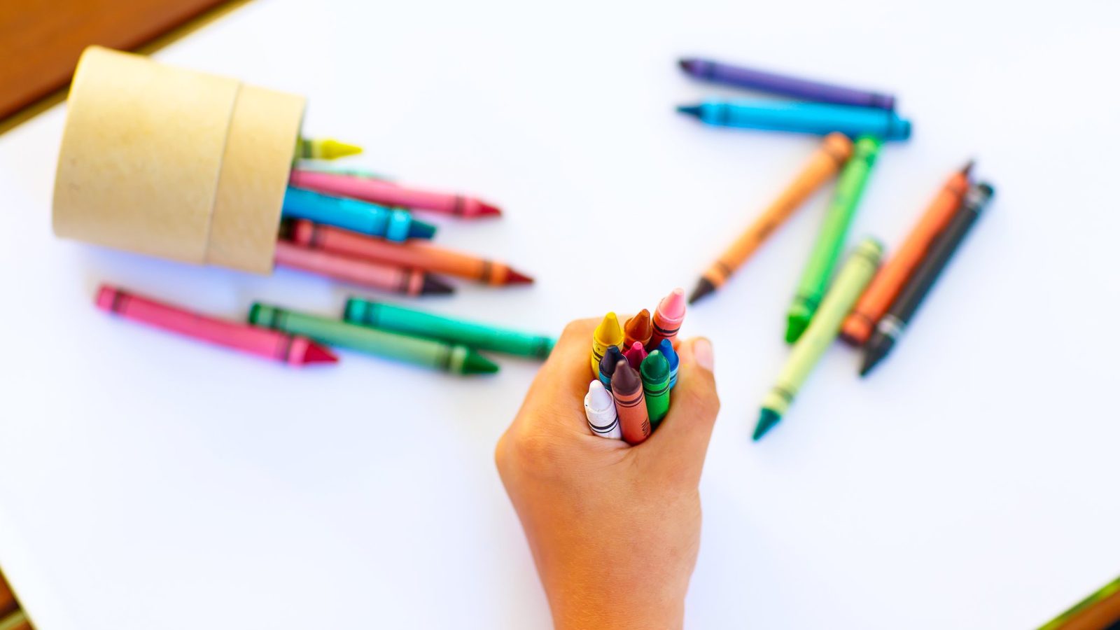 Hand holding crayons above paper