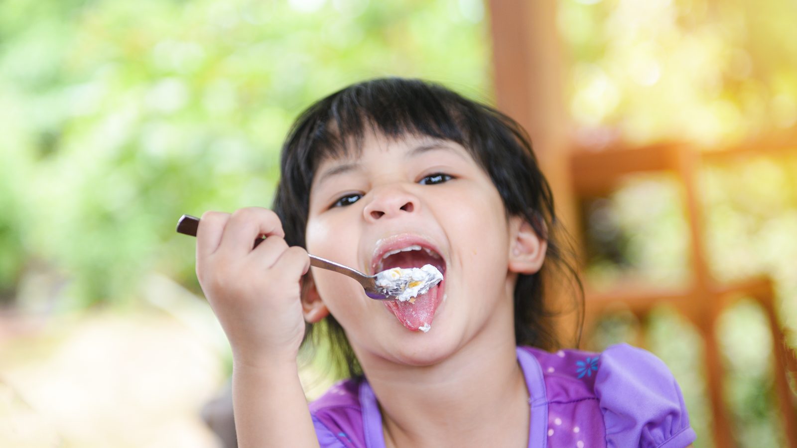 A girl laughing while eating with a spoon