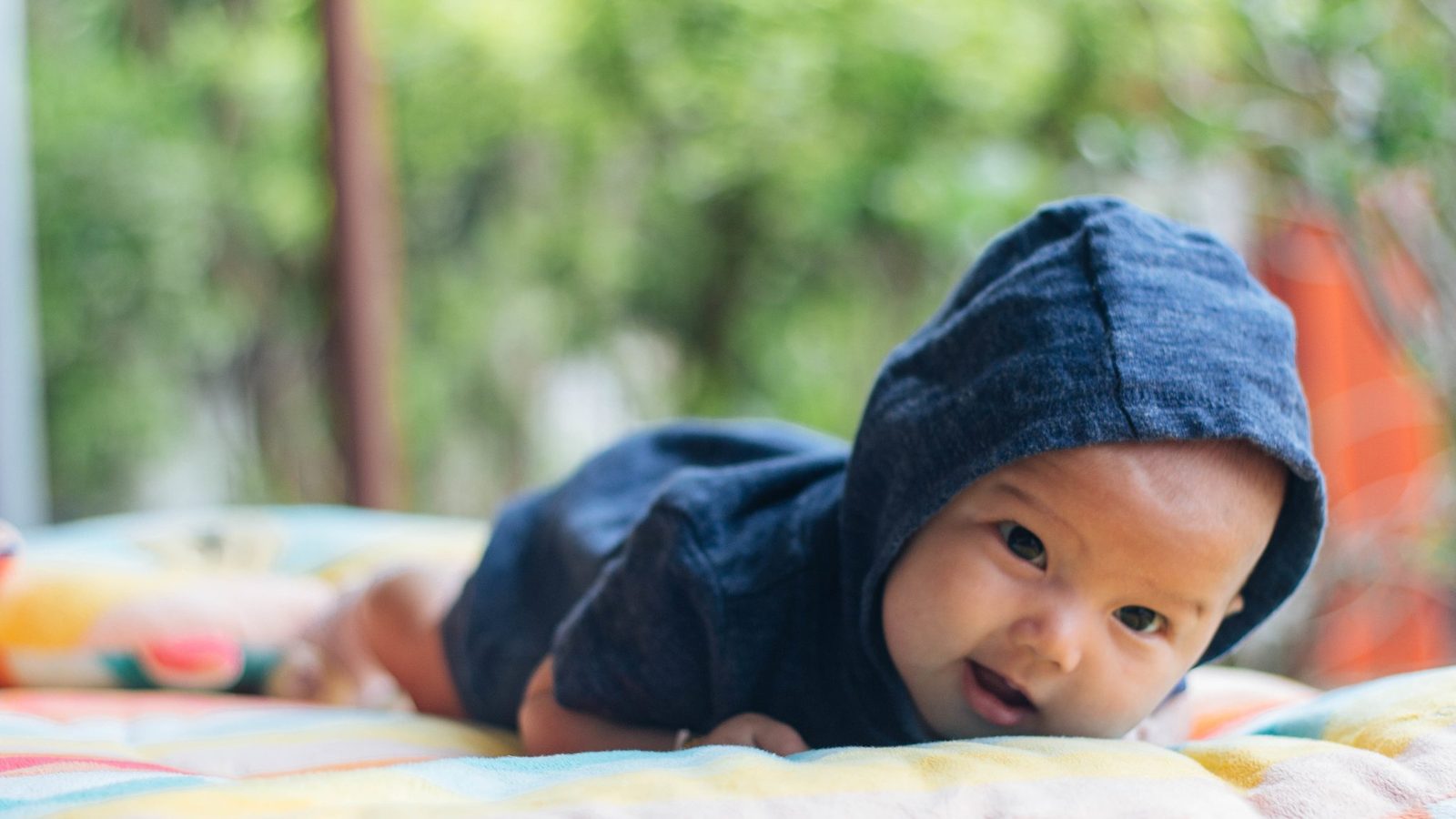 A baby in a hooded top crawling on a blanket