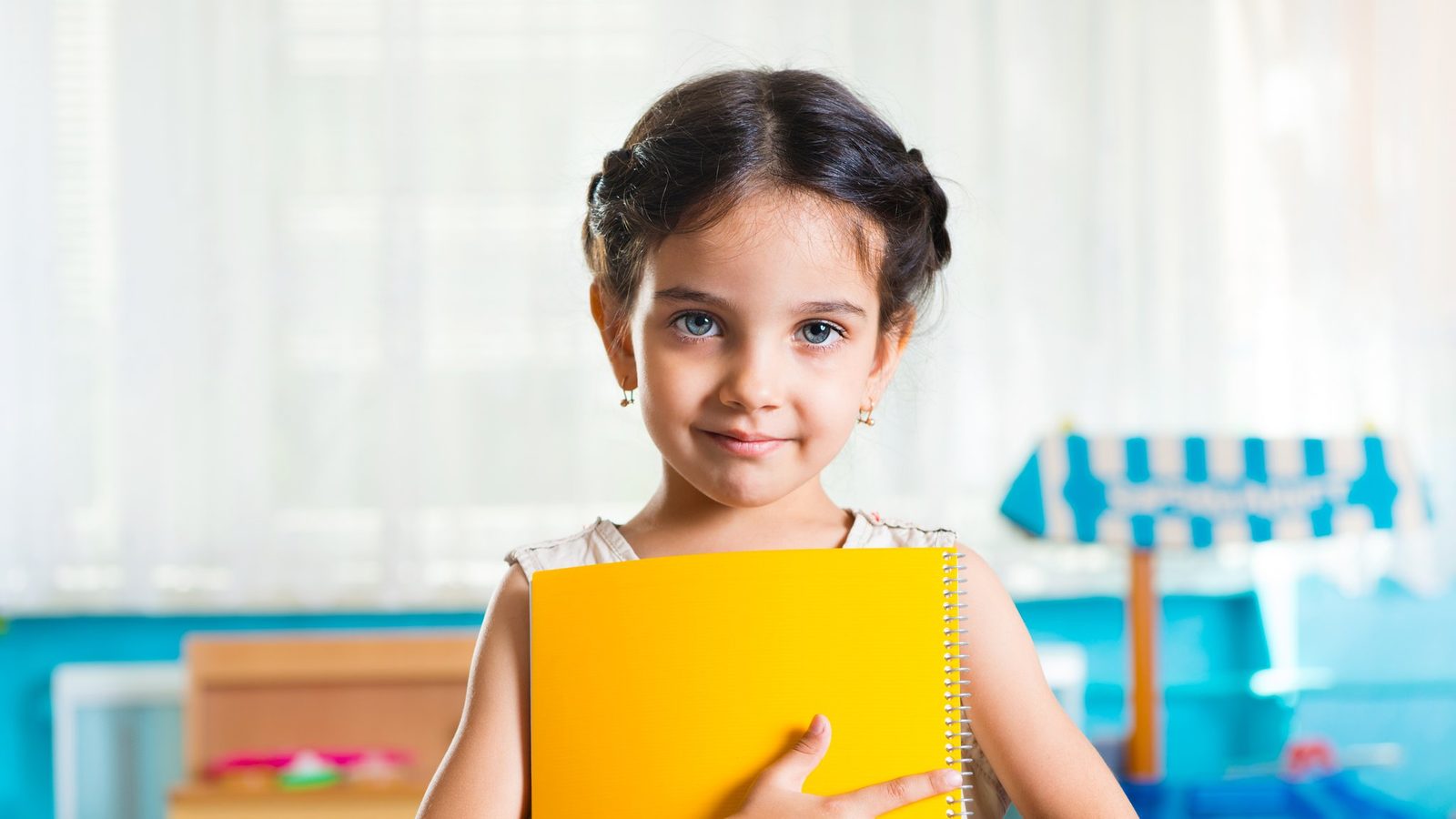 A smiling girl holding a yellow folder in a classroom