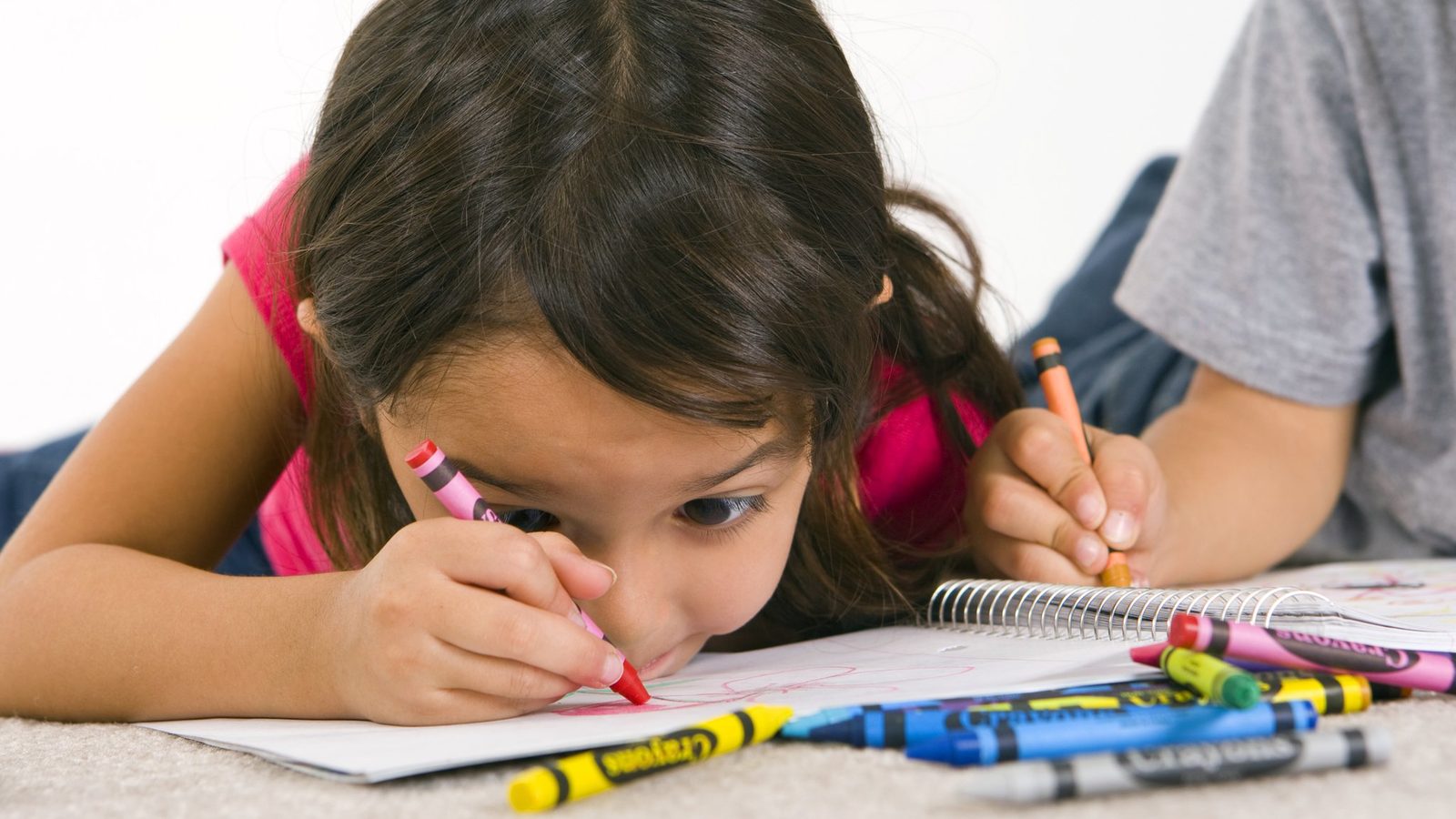 A girl drawing with crayons on the floor