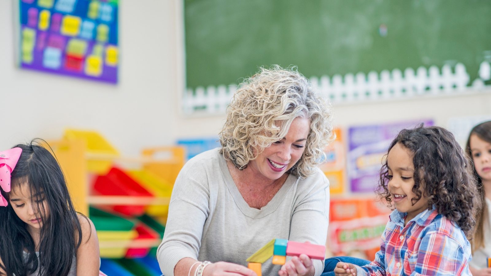 A teacher building with blocks alongside preschool children