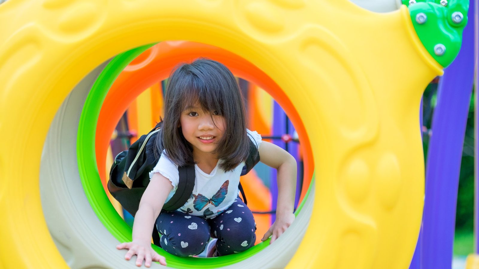 A toddler peeking through a colourful play tunnel