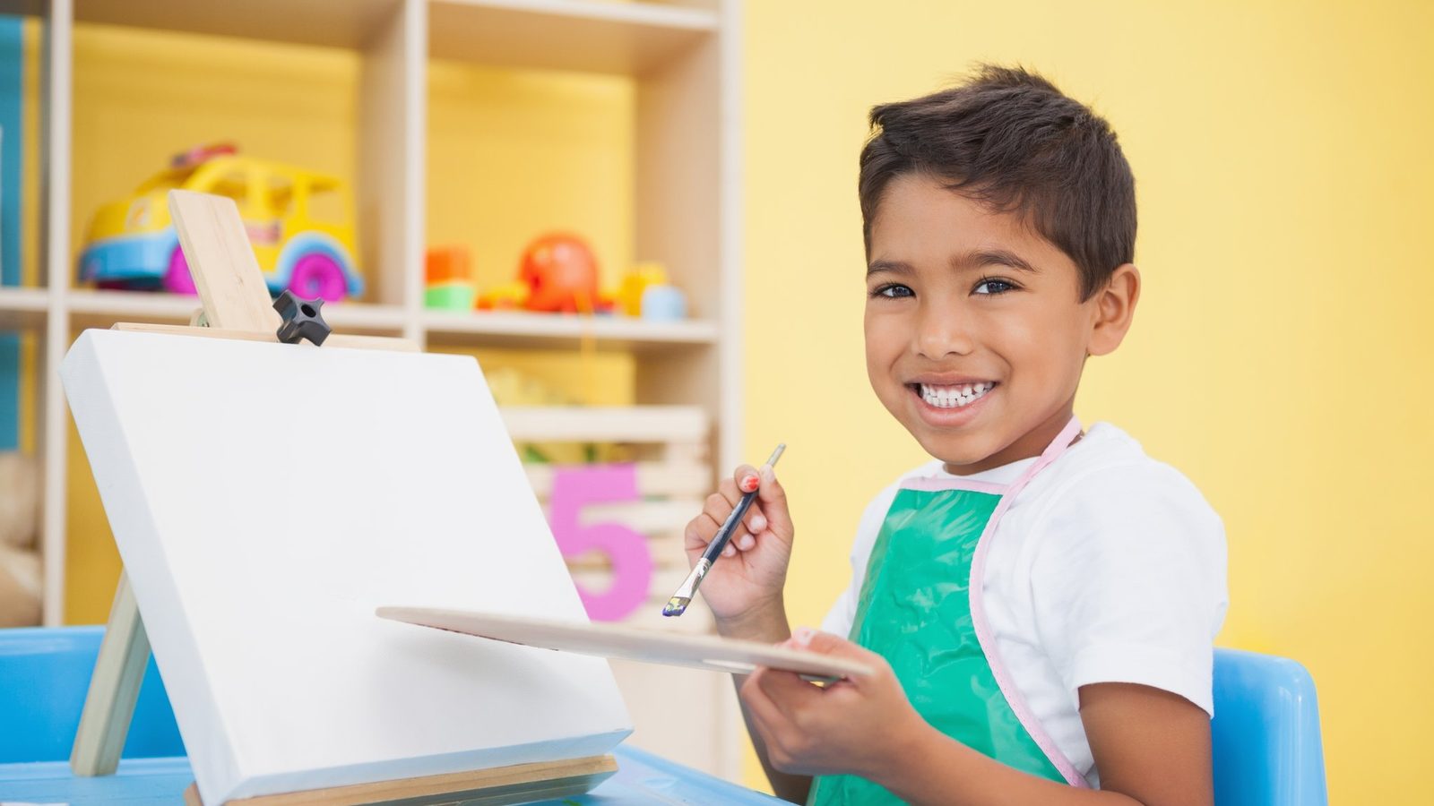 A boy painting at an easel in a classroom