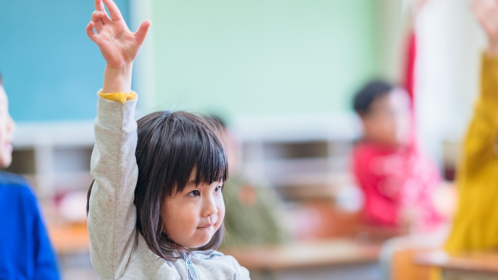 A young girl raising her hand in class