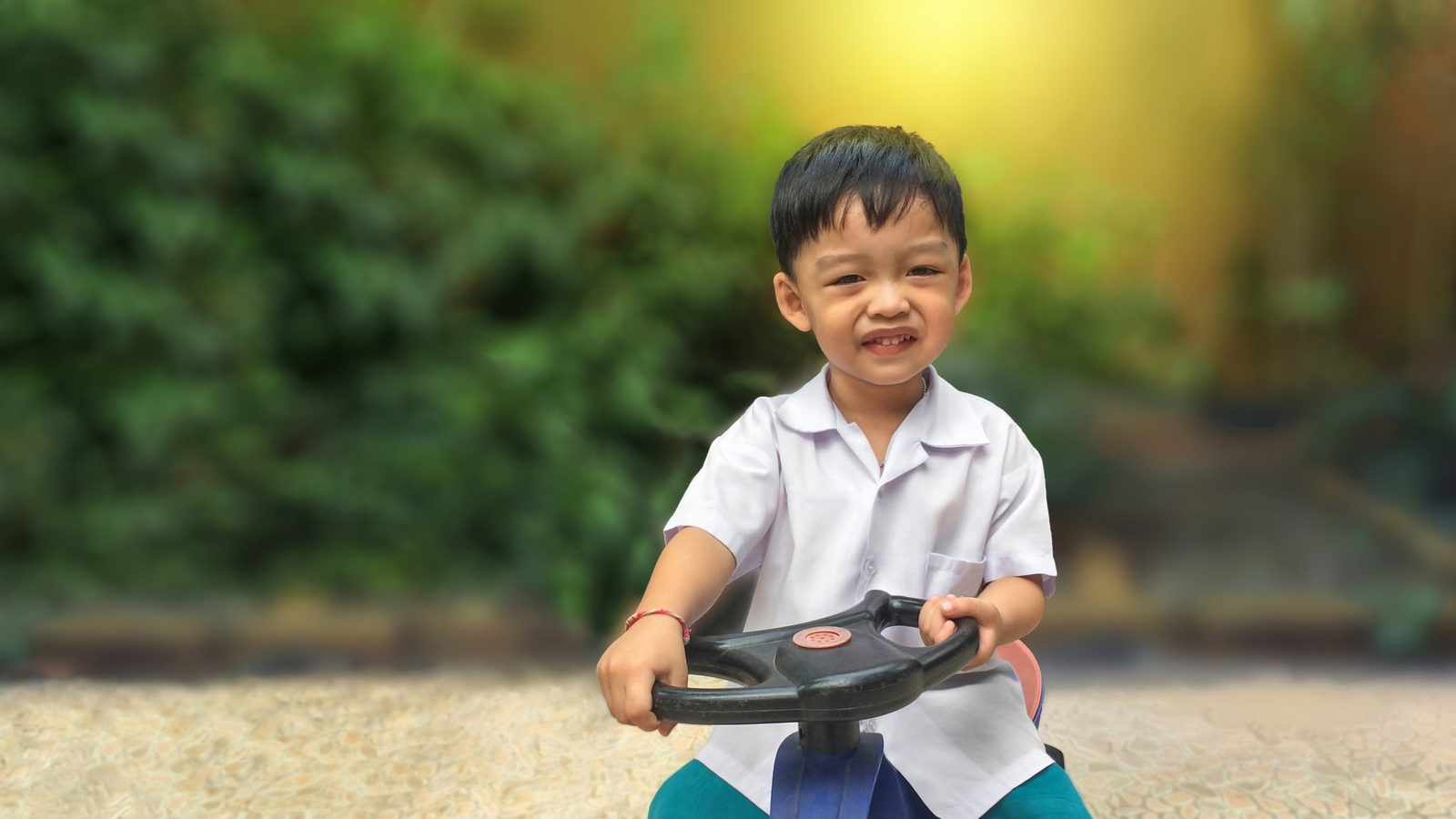 A smiling boy riding a toy outdoors