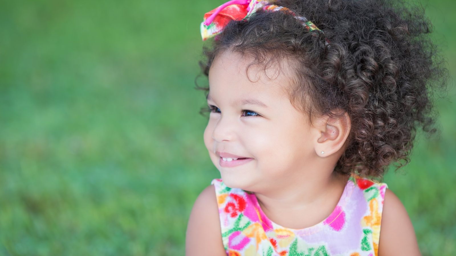 A smiling toddler with curly hair outdoors