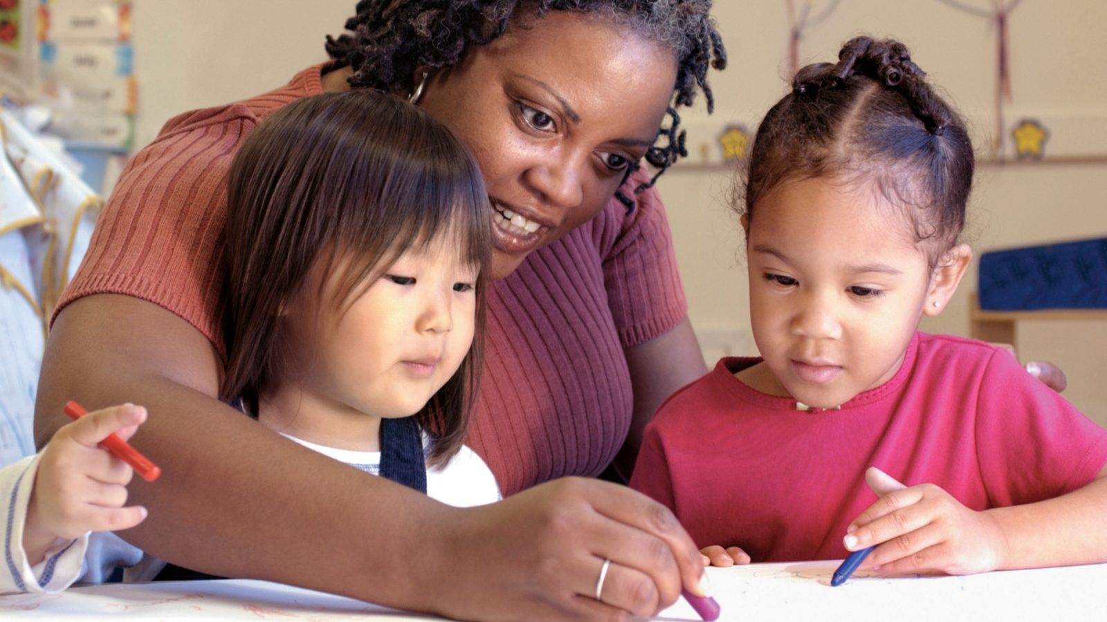 A teacher helping preschool girls with an art activity