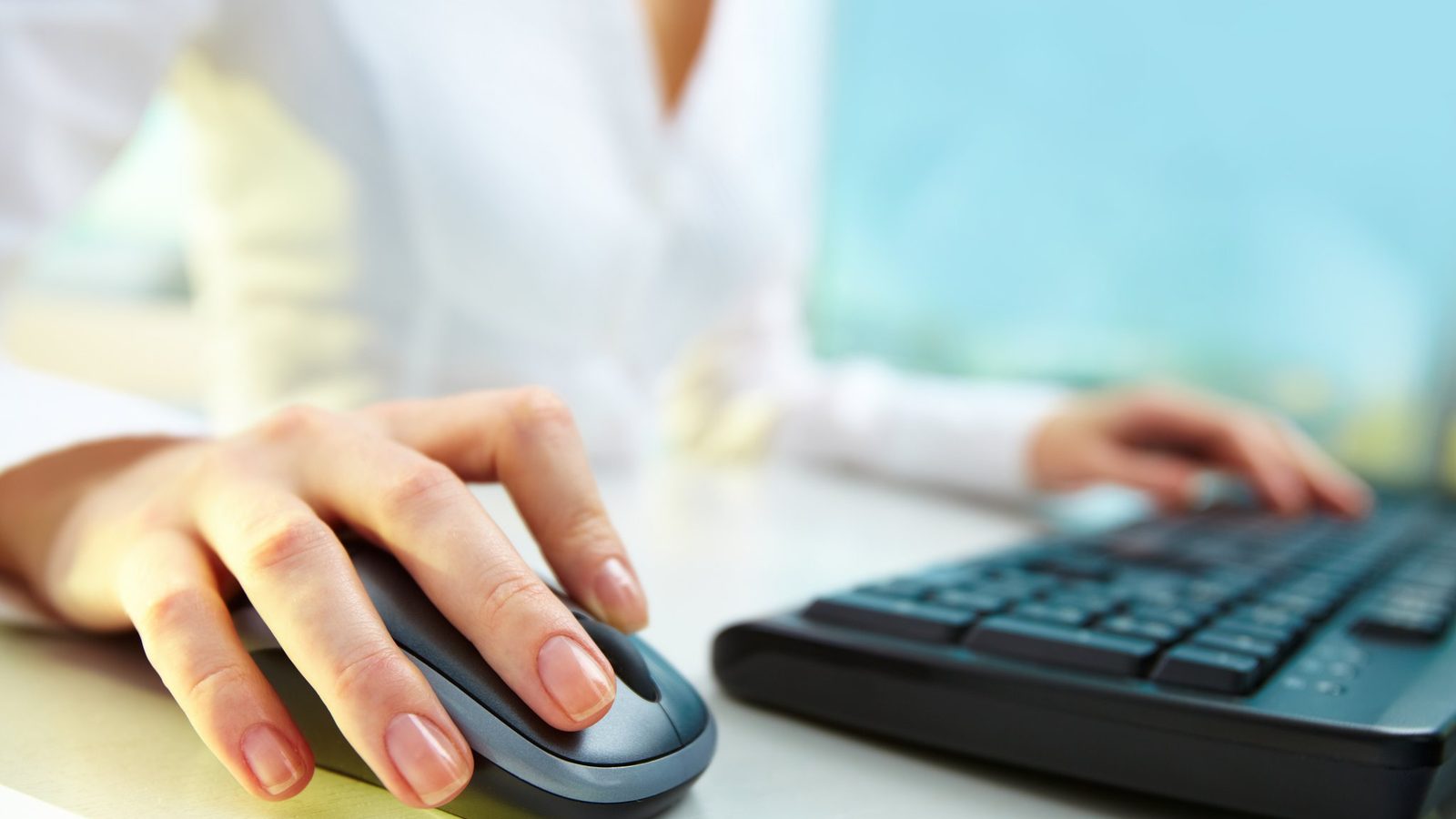 Hand using a computer mouse beside a keyboard