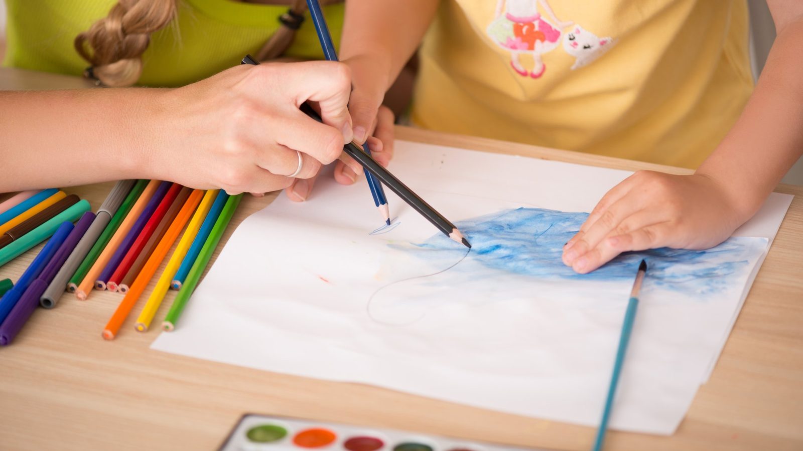 Hands painting with watercolours and coloured pencils
