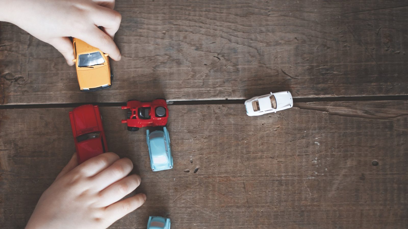 Hands playing with toy cars on a wooden floor