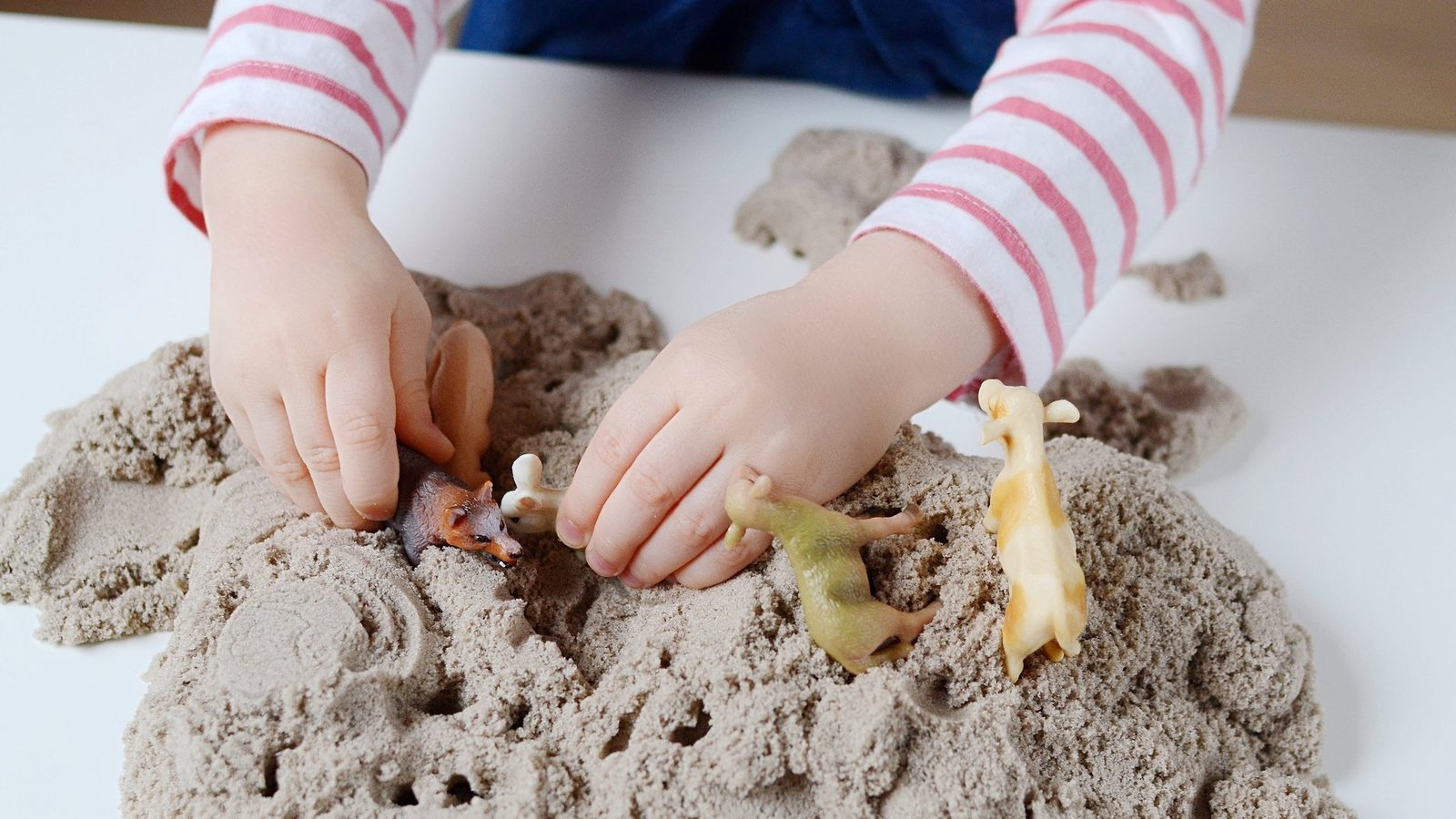 Hands playing in sand with small toys